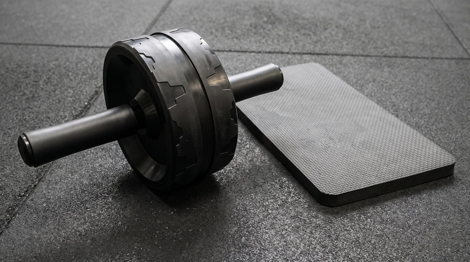 A wide ab roller with two handles beside a kneeling pad.
