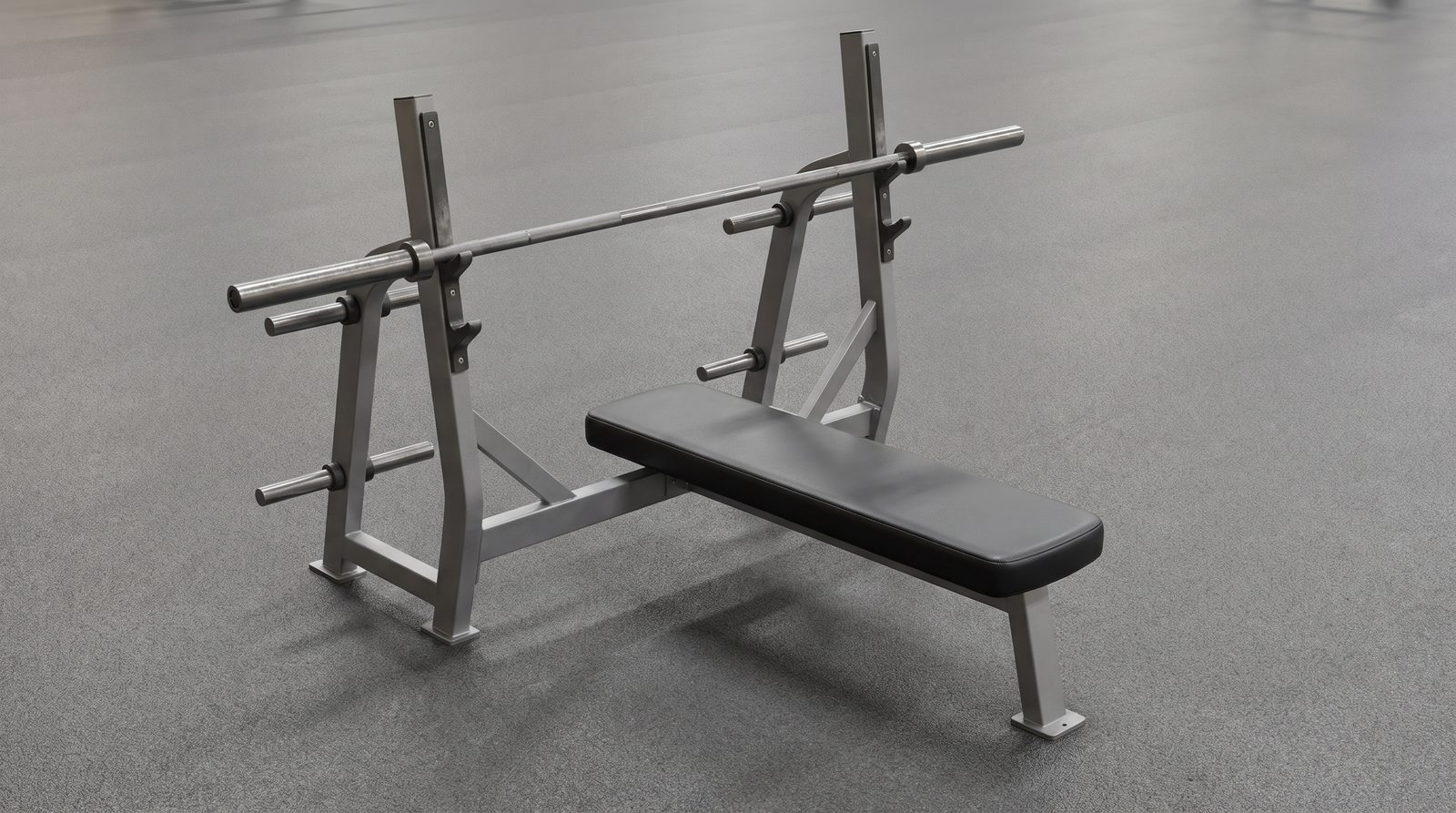 An empty flat bench aligned beneath a barbell supported on paired uprights.