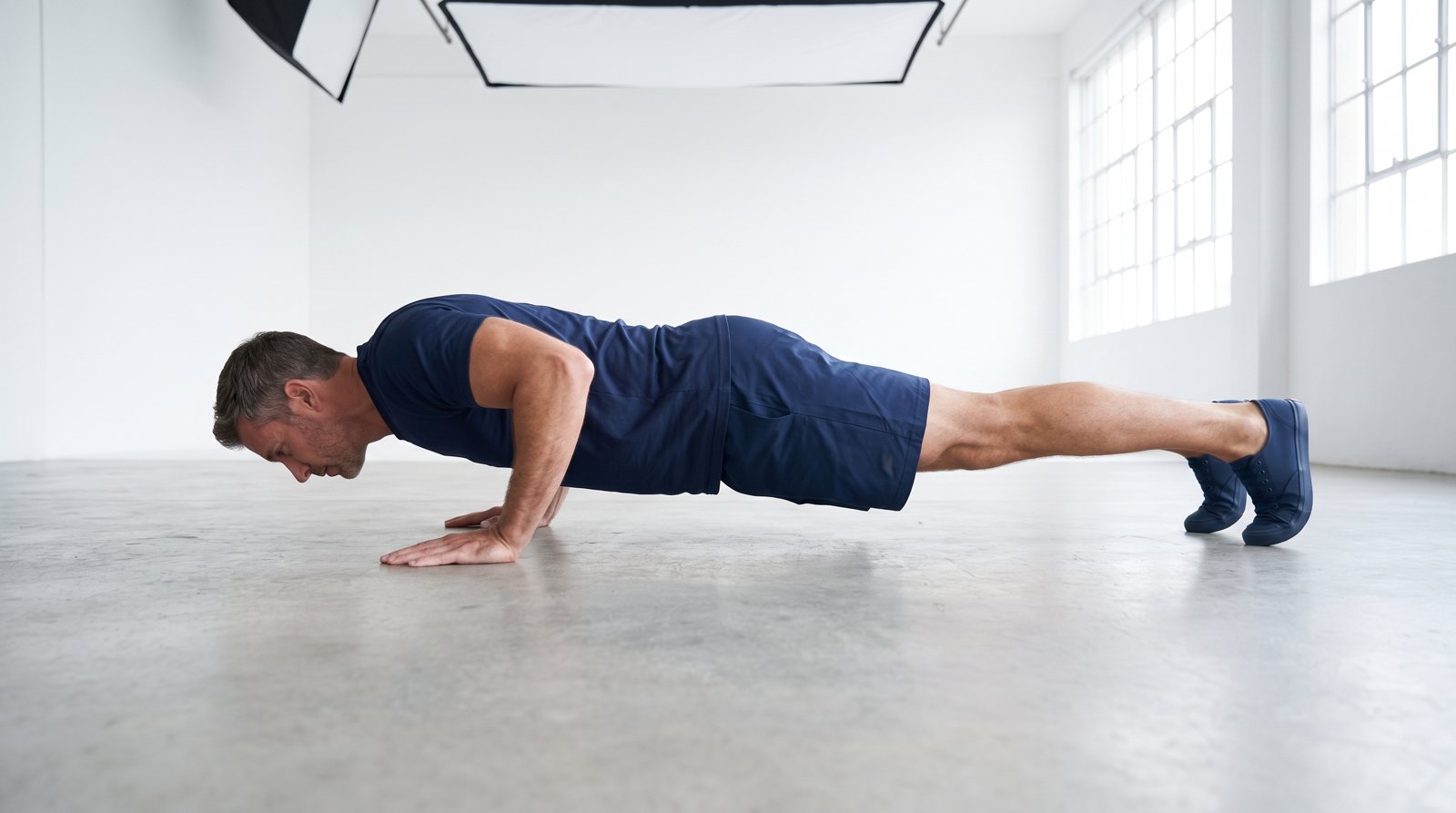 An adult in a lowered push-up position on a clear exercise floor.