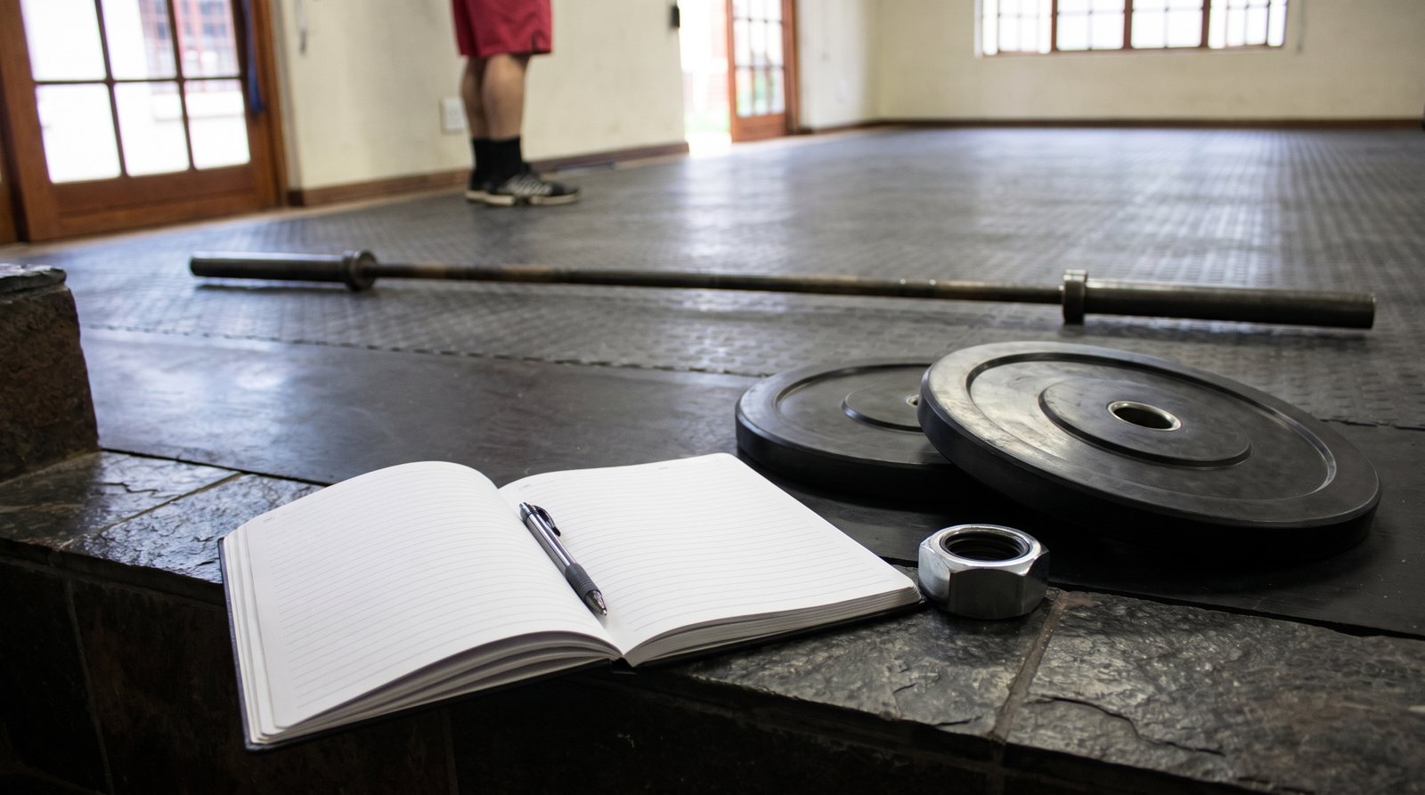 A blank workout log beside smooth weight plates and a bar collar.