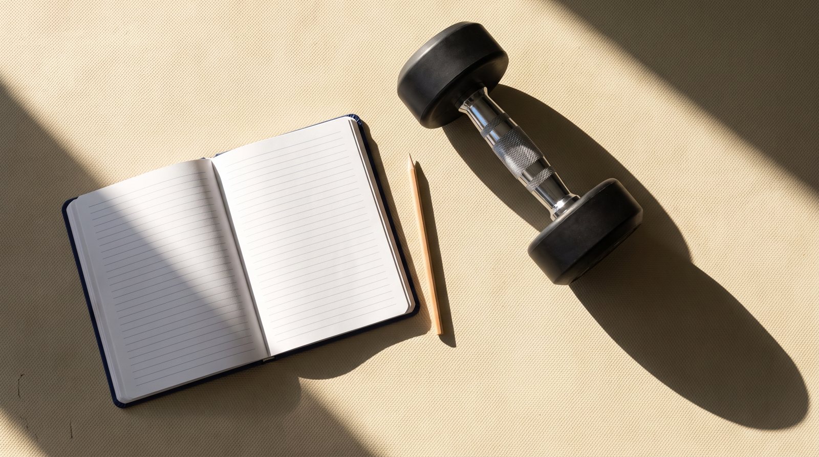 A blank workout notebook beside one smooth dumbbell.