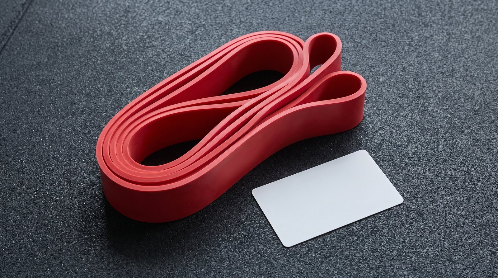 A long closed resistance band partly coiled beside a plain inspection card.