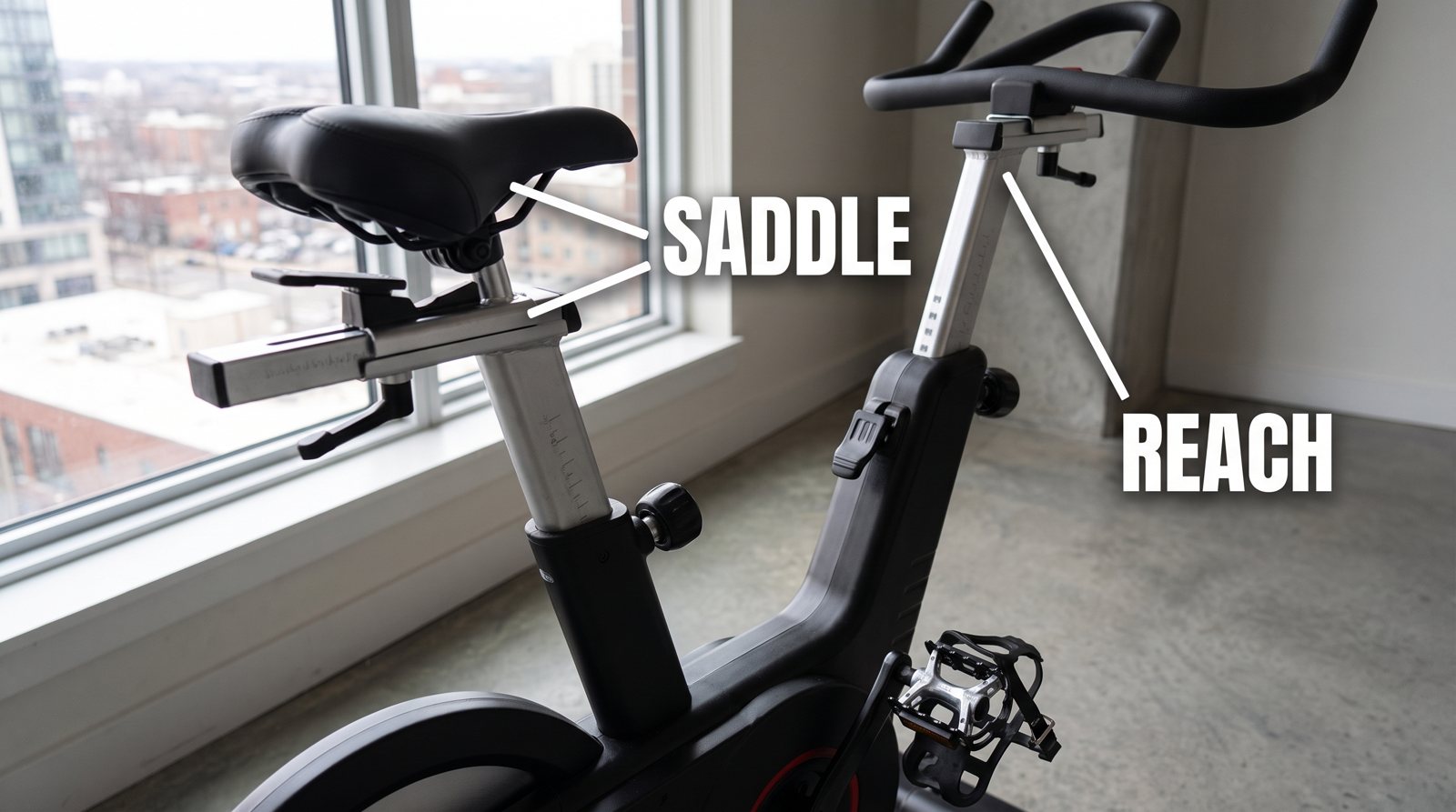 A close view of a spin bike saddle and handlebar adjustments, labelled saddle and reach.