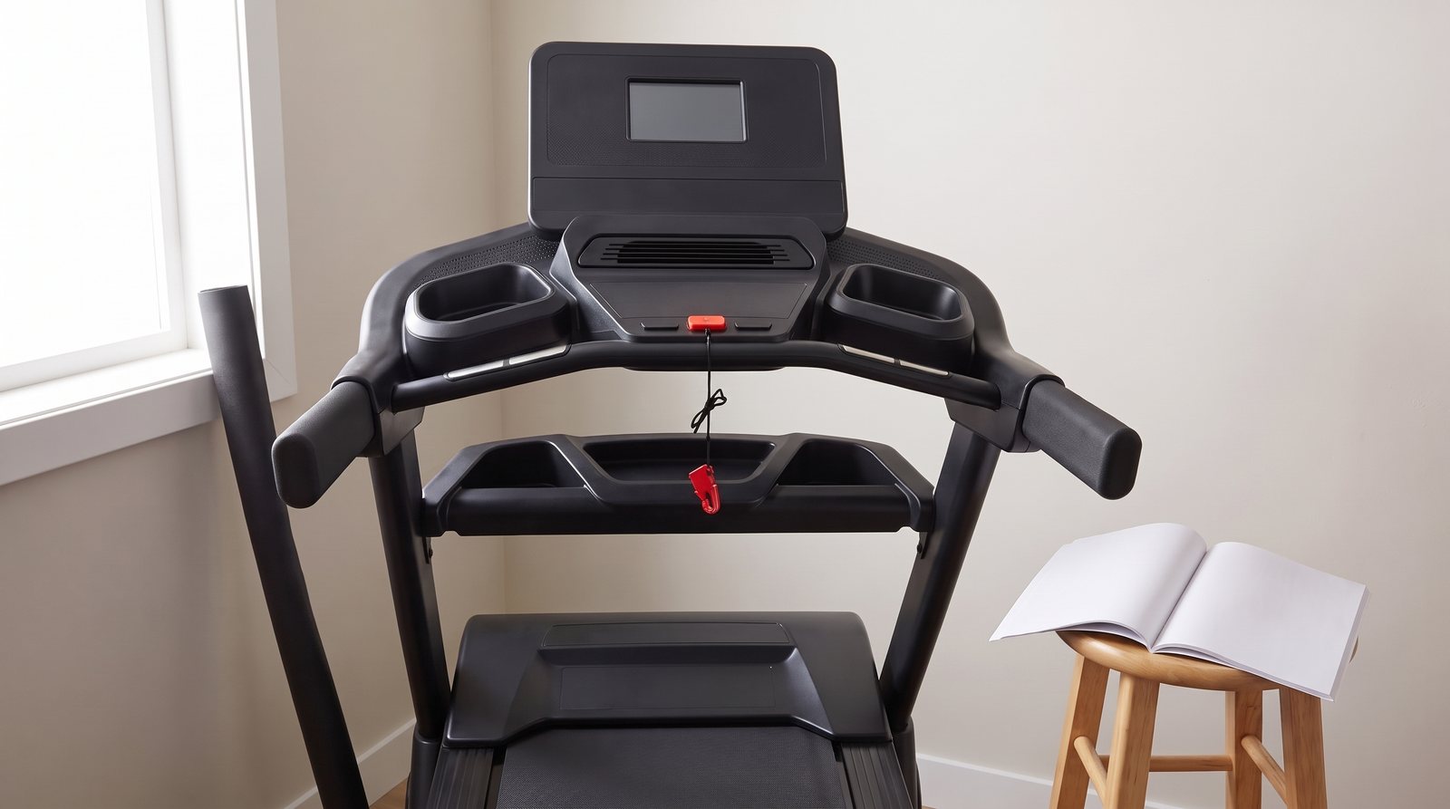 A treadmill console and handrails with one attached safety tether beside an open manual.