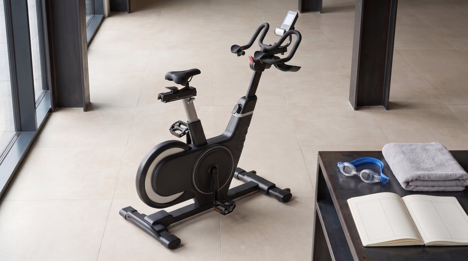 An indoor bike beside swimming goggles, a towel and blank training plan.